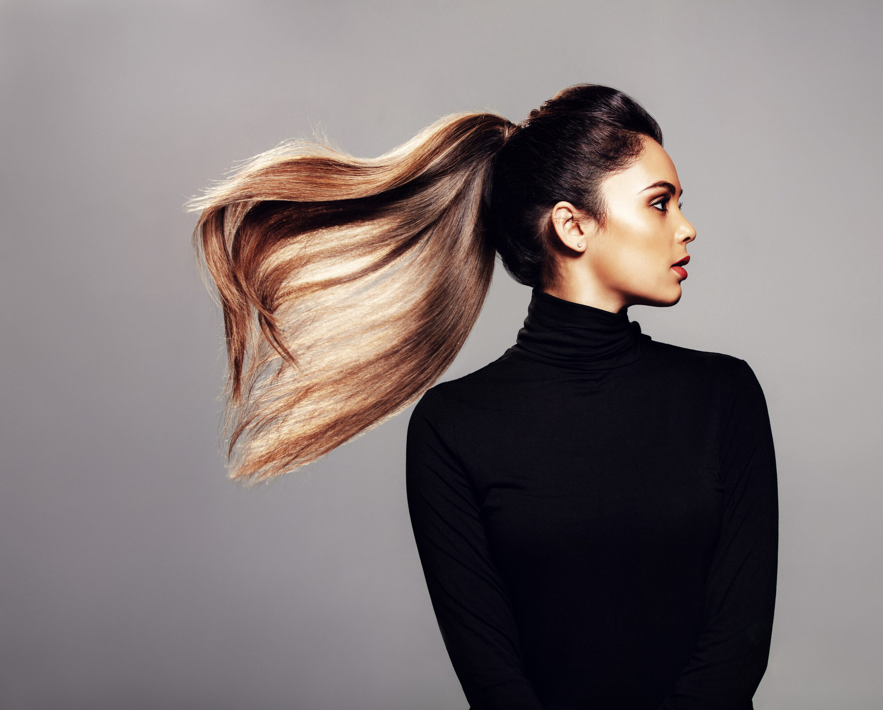 Studio shot of stylish young woman with flying hair against grey background. Female fashion model with long hair.